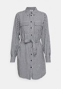 Vestido cambray a cuadros en blanco y negro con mangas largas, cierre de botones en la parte frontal, dos bolsillos en el pecho y una cinturilla anudada para un ajuste ajustable.
