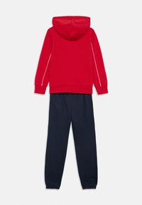 Κόκκινο βαμβακερό φούτερ με κουκούλα και λευκές ρίγες στα πλευρά, σε συνδυασμό με ναυτικό μπλε φόρμα με ελαστικές μανσέτες και άνετη εφαρμογή.