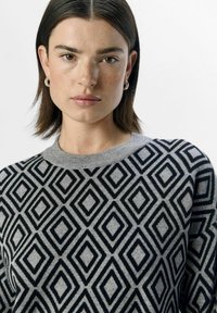 Grauer Pullover mit einem Rautenmuster in Schwarz und Hellgrau. Runder Halsausschnitt und gerippte Details. Weicher Stoff.