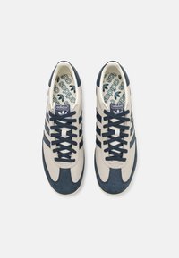 Beige en marineblauwe sneakers van leer en suede met een design van drie strepen, ronde neus, platte zool en gemusterde binnenzolen.