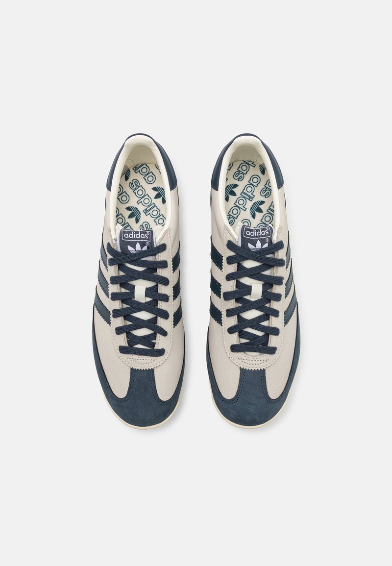 Beżowe i granatowe sneakersy wykonane ze skóry i zamszu, z designem w trzy paski, okrągłym noskiem, płaską podeszwą i wzorzystymi wkładkami.