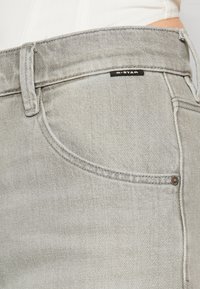 Szare dżinsy z denimu o lekko postarzanej fakturze, wyposażone w przednią kieszeń, jasne przeszycia oraz czarną etykietę na pasku talii.