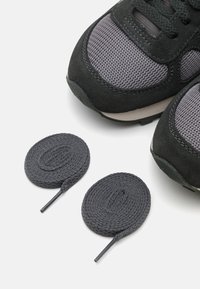 Sportschuhe in Schwarz und Grau, mit einem Obermaterial aus Mesh und Wildleder, dicken Schnürsenkeln und einer gepolsterten Sohle. Die Schnürsenkel werden separat angezeigt.