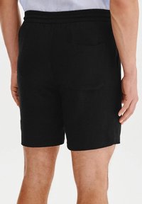 Czarne spodenki z elastycznym paskiem w talii, jedną tylną kieszenią i gładką fakturą, o długości sięgającej do połowy uda.