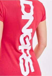 Red cotton t-shirt featuring bold white text vertically aligned on the back. Short sleeves and a soft texture complete the design.