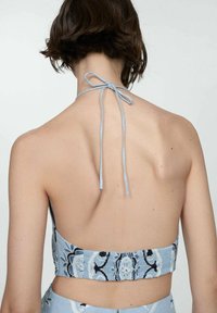 Top halter scurt, cu un model albastru, care se leagă la spate. Materialul texturat are motive florale în nuanțe mai deschise și mai închise.
