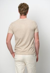 Ljusbrun t-shirt med korta ärmar, tillverkad av ett mjukt, strukturerat material. Den har en rund halsringning och en avslappnad passform med sidslitsar.