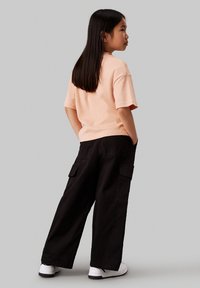 Lichtroze katoenen t-shirt met korte mouwen, gecombineerd met loszittende zwarte cargobroek met zijzakken en witte sneakers.