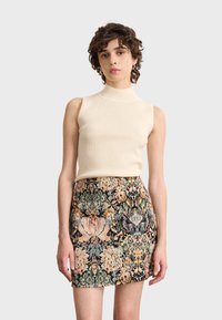 Top sin mangas color crema de canalé combinado con una falda corta multicolor con estampado floral, que presenta texturas y un detallado intrincado.