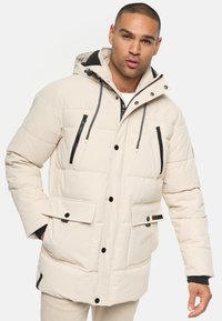 Beige pufferjakke med hætte, med sorte lynl�åslommer, frontlommer med trykknap og kontrastfarvede snore.