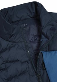 Giacca imbottita blu scuro con cerniera frontale parzialmente aperta e collo visibile, che mostra la fodera interna e una patta di tasca blu.