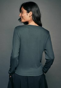Mørkegrøn langærmet top med ribbet tekstur, rund halsudskæring og tætsiddende design. Styllet med en flydende sort nederdel.