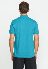 T-Shirt mit kurzen Ärmeln und Kragen in Teal, aus strukturiertem Stoff. Mit geradem Saum und Rückennaht. Kombiniert mit dunklen Shorts.