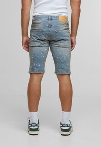 Traper šortsevi svijetloplave boje sa istrošenim deteljama i bijelim prskanjem, te smešnom kožnom etiketom na pojasu.