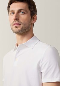 Polo bianco a maniche corte con colletto classico e chiusura a un bottone. Texture liscia, vestibilità su misura e leggero lucido.