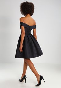 Black off-shoulder dress with a fitted bodice, flared skirt, and silky texture, complemented by a zipper closure and pleated detailing.