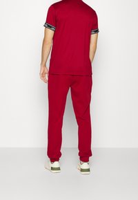 Rote Sportbekleidung mit einem Kurzarmshirt und passenden Jogginghosen. Das Shirt hat schwarze Akzentstreifen an den Ärmeln.