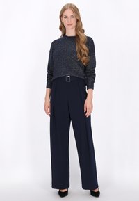 Pulover bleumarin cu fir metallic, design scurt; asortat cu pantaloni largi bleumarin, cu talie înaltă, având un detaliu cu cataramă. Tocuri negre.
