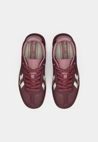 Ζευγάρι μπορντό σουέντ αθλητικά παπούτσια με λευκές ρίγες στο πλάι και κορδόνια, φαίνονται από πάνω σε ουδέτερο φόντο.