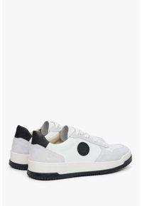 Białe trampki wykonane z zamszu i skóry, z fakturowanymi akcentami, okrągłą naszywką z logo oraz kontrastującym czarnym obcasem i podeszwą.