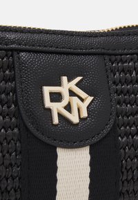 Bolso de mano tejido en negro con un material texturizado, una solapa de cuero negro y un logo en tono dorado "DKNY". Rayas delgadas en crema acentúan el diseño.