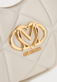 Geantă din quilt de culoare bej deschis, cu un logo auriu strălucitor și inscripția "LOVE MOSCHINO", având o textură netedă și închidere cu fermoar.