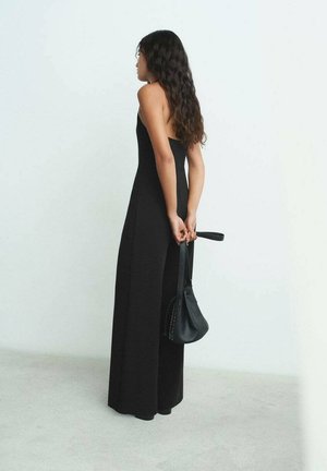 Jumpsuit nero senza maniche con corpetto aderente e design a gamba larga, abbinato a una piccola borsa nera con tracolla.