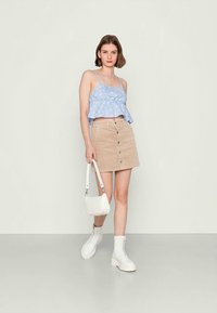 Top sem mangas azul claro com padrão floral branco, combinado com uma saia mini de veludo côr de bege com botões na frente, acessorizado com uma bolsa branca e botas.