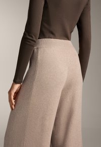 Ljust beige vida byxor med ribbad midjeband och texturerade paneldetaljer, tillverkade av mjukt och bekvämt material.