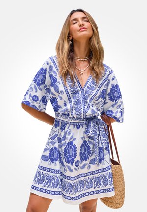 Vestito a maniche corte bianco con motivi floreali blu e disegni paisley. Presenta una scollatura a v e una cintura annodata. Include una borsa intrecciata.