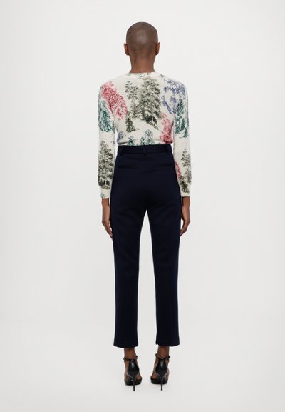 Long-sleeve, cream sweater with colorful tree patterns, paired with tailored dark navy trousers and black heeled shoes, viewed from behind.