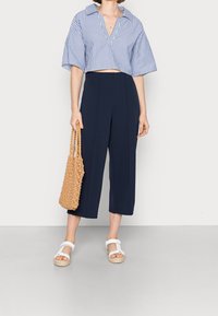 Tajt blå och vit randig skjorta med breda ärmar, i kombination med marinblå vida byxor och vita sandaler. Håller en vävd beige väska.