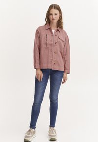 Roza denim jakna z gumbi, prsni žep in zadrgo. Kombinirana z modrimi skinny jeans in bež supergami.