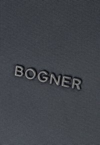 Schwarzer Stoff mit Struktur und erhabenen Buchstaben "BOGNER" in glatter Ausführung, mittig vor einem grauen Hintergrund.