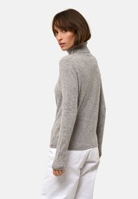 Šedý, přiléhavý rolák vyrobený z měkkého materiálu, s dlouhými rukávy a žebrovaným límcem, kombinovaný s bílými kalhotami.