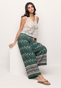Crochet-style white cropped tank top with a v-neck. Green wide-leg pants feature zigzag and geometric patterns in purple and white.