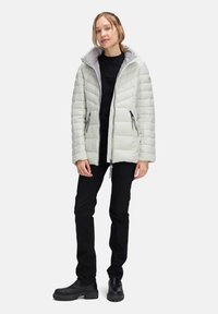 Jasnoszara kurtka puchowa z poziomym pikowaniem, szarym podbiciem wewnętrznym, z przodu na zamek błyskawiczny i dwiema bocznymi kieszeniami. W zestawie z czarnymi spodniami i butami.