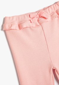 Vaaleanpunaiset ribbirekkarit, joissa on röyhelövyötärö ja nauhakoriste. Kangas on pehmeä ja sileä, ja ne ovat vartalonmyötäiset.
