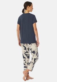Marineblaues Kurzarmoberteil, kombiniert mit cremefarbenen Hosen mit großem Blattmuster. Das Outfit besteht aus einem weichen, leichten Stoff.