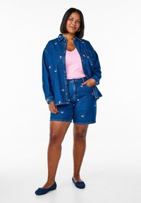 Conjunto de chaqueta de denim y pantalones cortos en azul oscuro con bordados florales, combinado con una blusa de cuello en V de color rosa claro y zapatos planos azules. Textura suave, diseño casual.