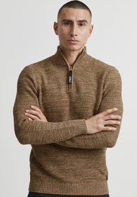 Maglione zip-up marrone con un design a maglia testurizzata, polsini e orlo a coste. Presenta una zip nera con logo.