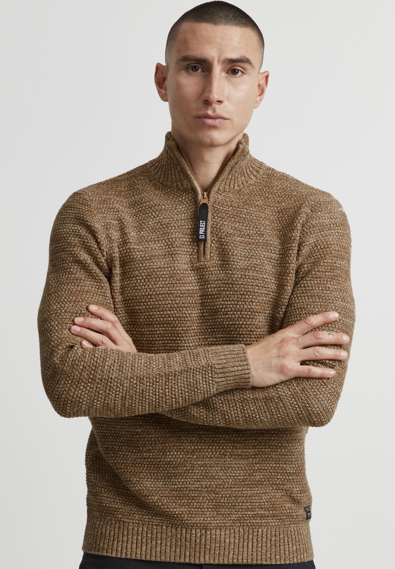 Maglione zip-up marrone con un design a maglia testurizzata, polsini e orlo a coste. Presenta una zip nera con logo.