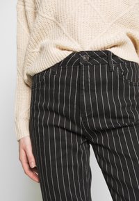 Svarta kostymbyxor med en figurnära passform, som har knappstängning och sidofickor, kombinerat med en texturerad krämfärgad tröja.