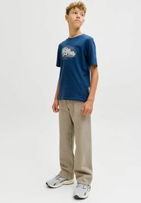 Camiseta de algodón azul marino con un estampado gráfico en blanco, combinada con pantalones beige claro y zapatillas grises. Cuello simple y mangas cortas.
