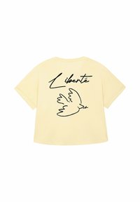 Een zachtgele t-shirt met een zwarte omtrek van een vogel die een olijftak vasthoudt en het woord "Liberté" in gestileerde letters erboven.