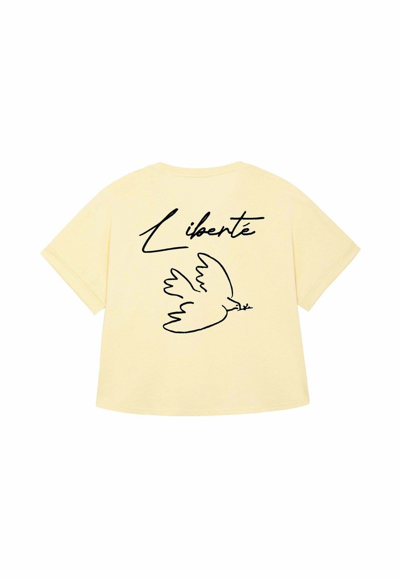 Een zachtgele t-shirt met een zwarte omtrek van een vogel die een olijftak vasthoudt en het woord "Liberté" in gestileerde letters erboven.