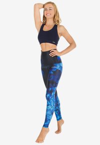 Hoge taille leggings in een blauwe geometrische patroon met zwarte accenten, gecombineerd met een marineblauwe sportbeha. Het materiaal lijkt rekbaar en aansluitend.