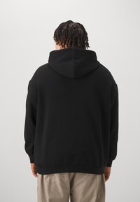 Czarny hoodie z kapturem o luźnym kroju, z ribbowanym dołem i mankietami, prezentowany z tyłu na neutralnym tle.
