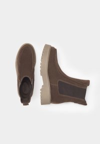 Bottines en daim marron avec une semelle en caoutchouc, des panneaux latéraux élastiques et des détails de couture. Surface texturée avec un design à bout arrondi.