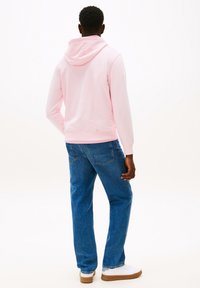 Felpa con cappuccio rosa, tessuto morbido, maniche lunghe e tasca a marsupio, abbinata a jeans in denim blu e sneakers bianche.